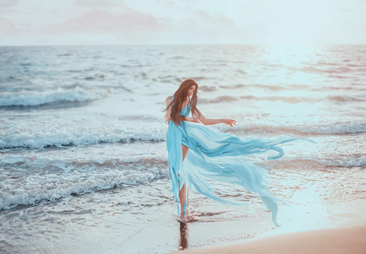 a pretty red-haired goddess in blue dress fluttering in the wind came from the depths to the shore