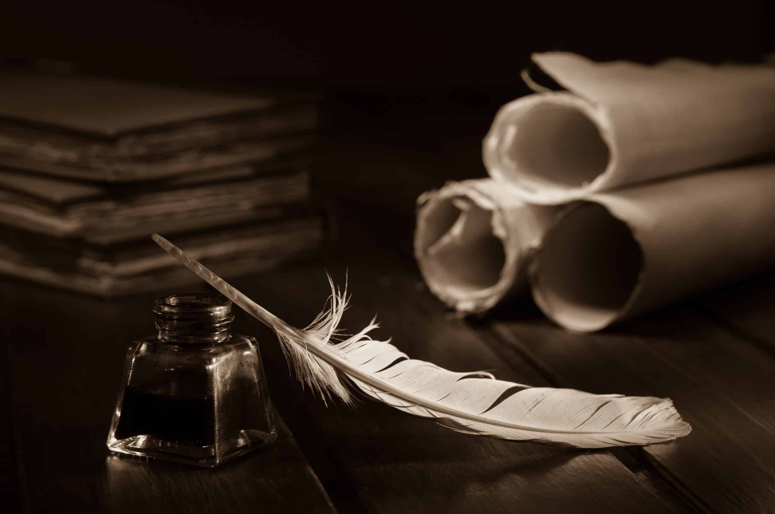 Quill pen, inkwell, and scrolls on wooden desk.