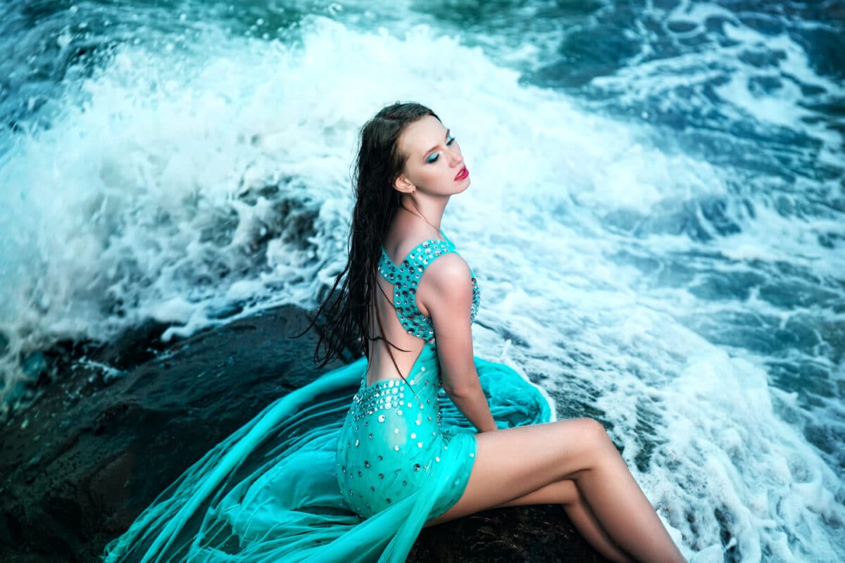 an enchantress sitting on a rock by the ocean