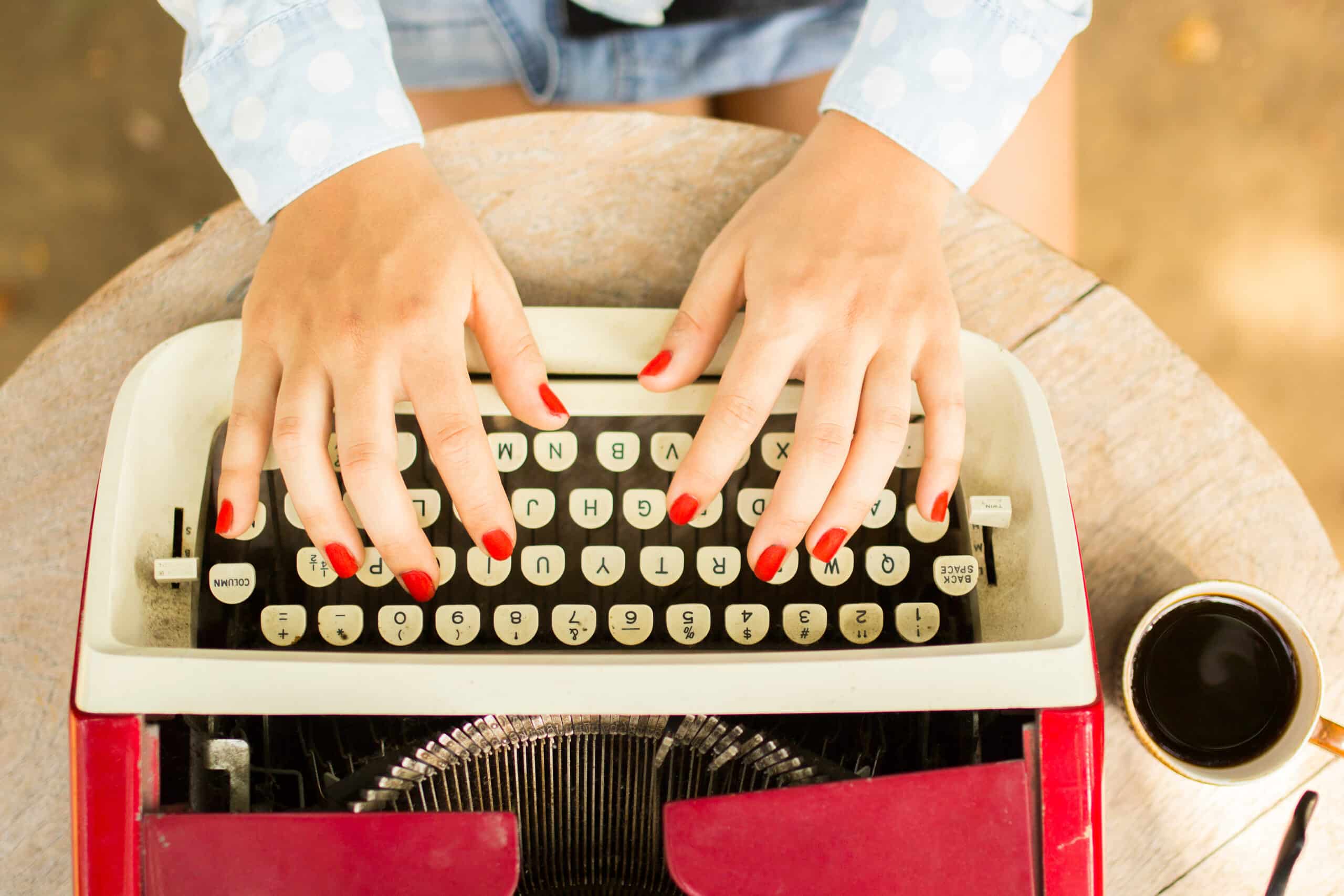 female hands with red nails typing on vintage typewriter