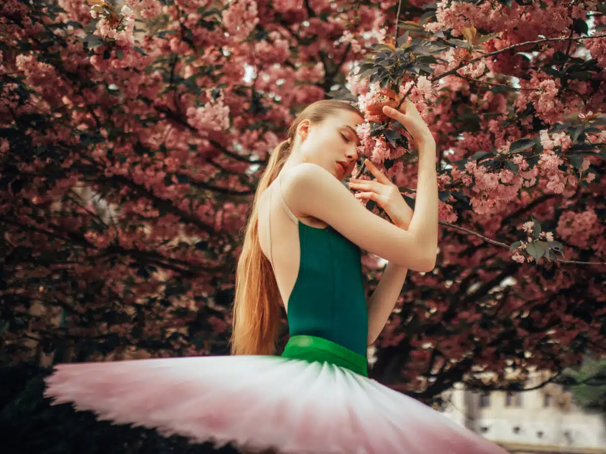 Ballerina is standing and enjoying next to flowering sakura tree