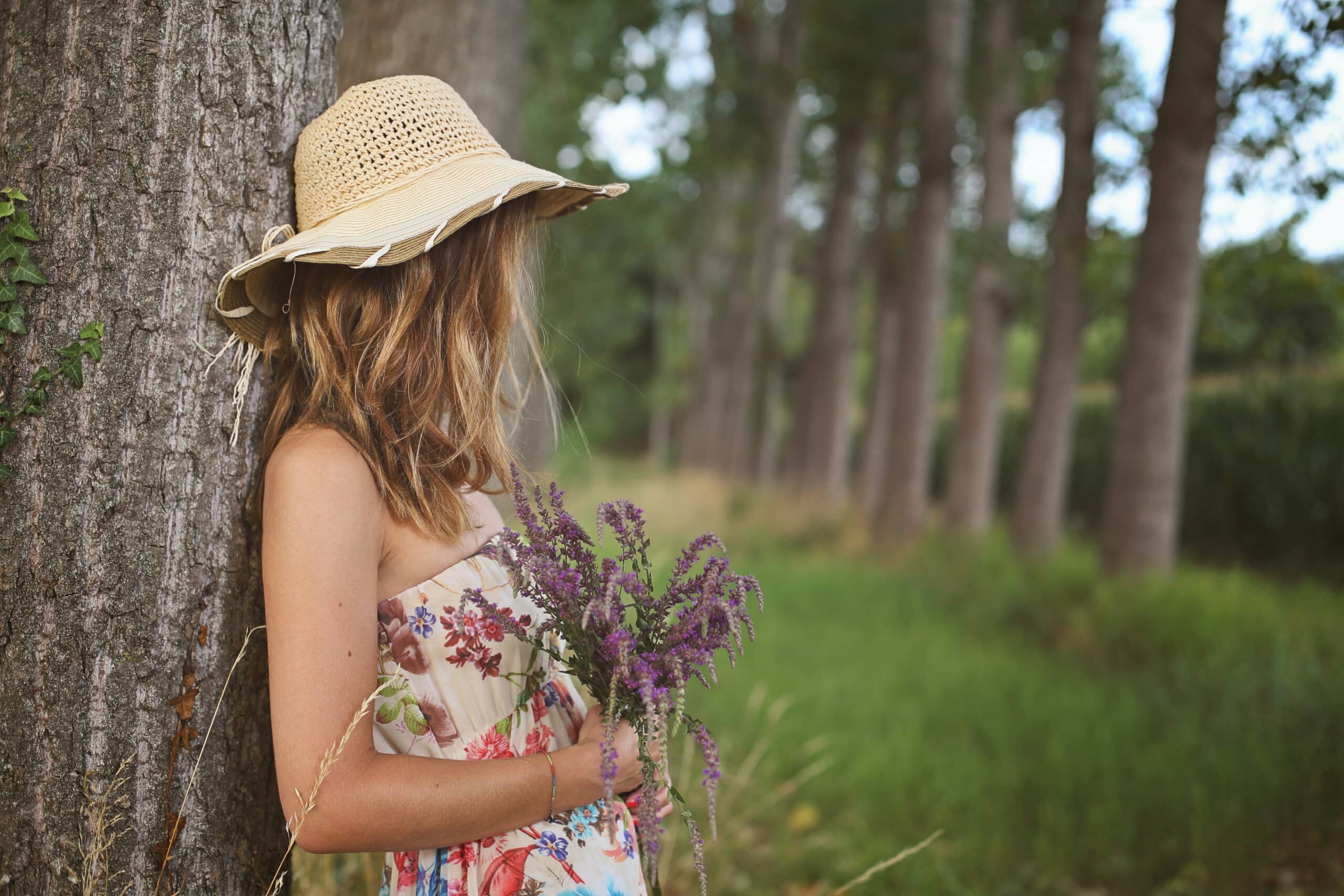 Young woman with wild flowers leaning against a tree in nature.