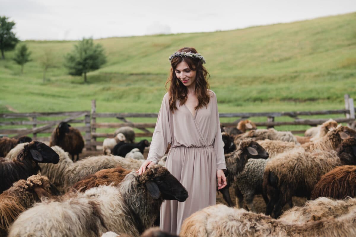 Beautiful, young and happy lady stands in the middle of a flock of sheep