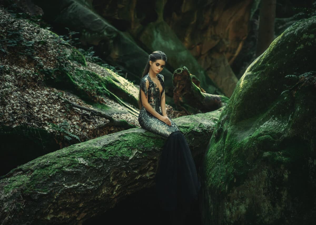 A young mysterious girl - a dark princess sits on a log among th