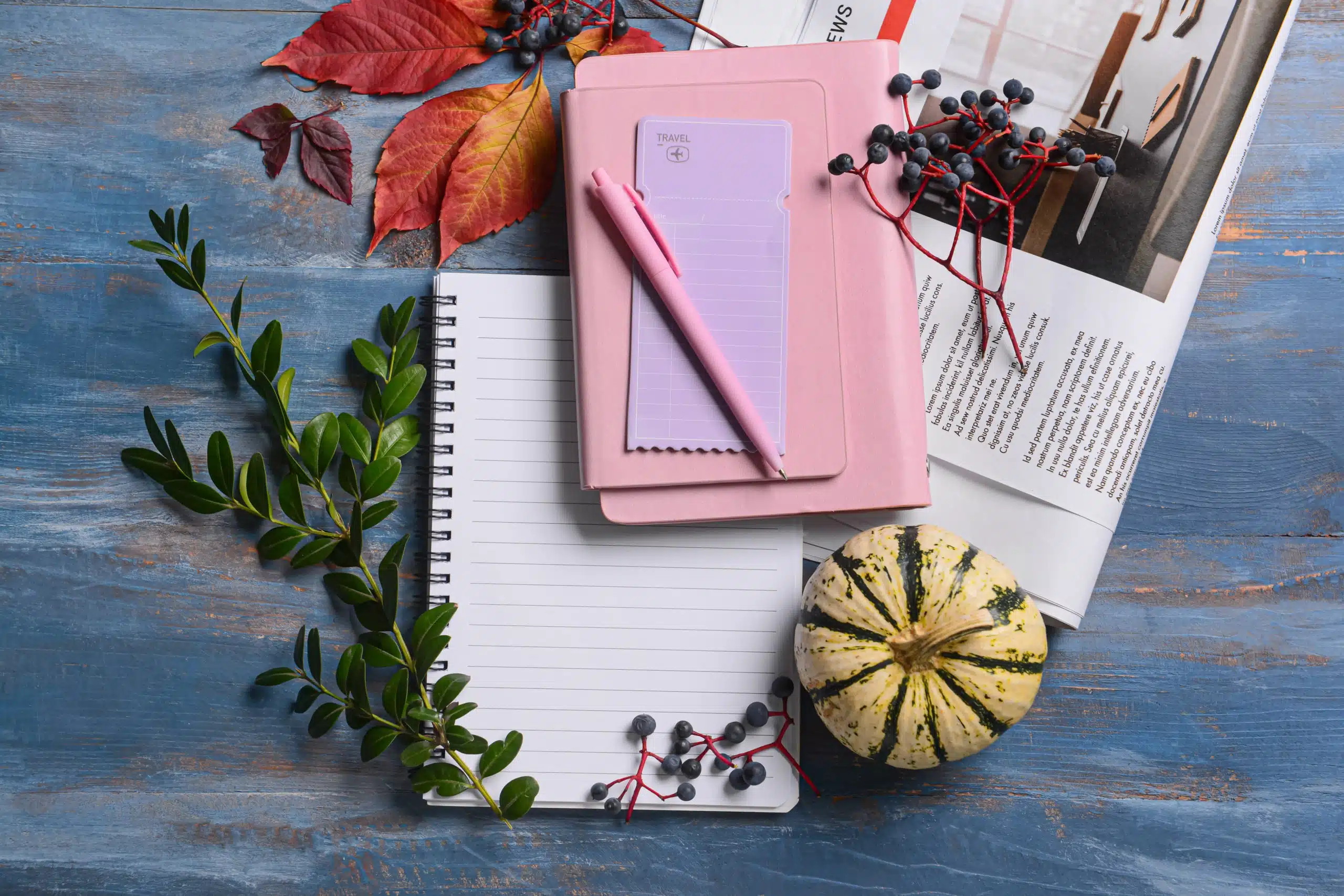 Notebooks with pen, newspaper and autumn decor on blue wooden background.