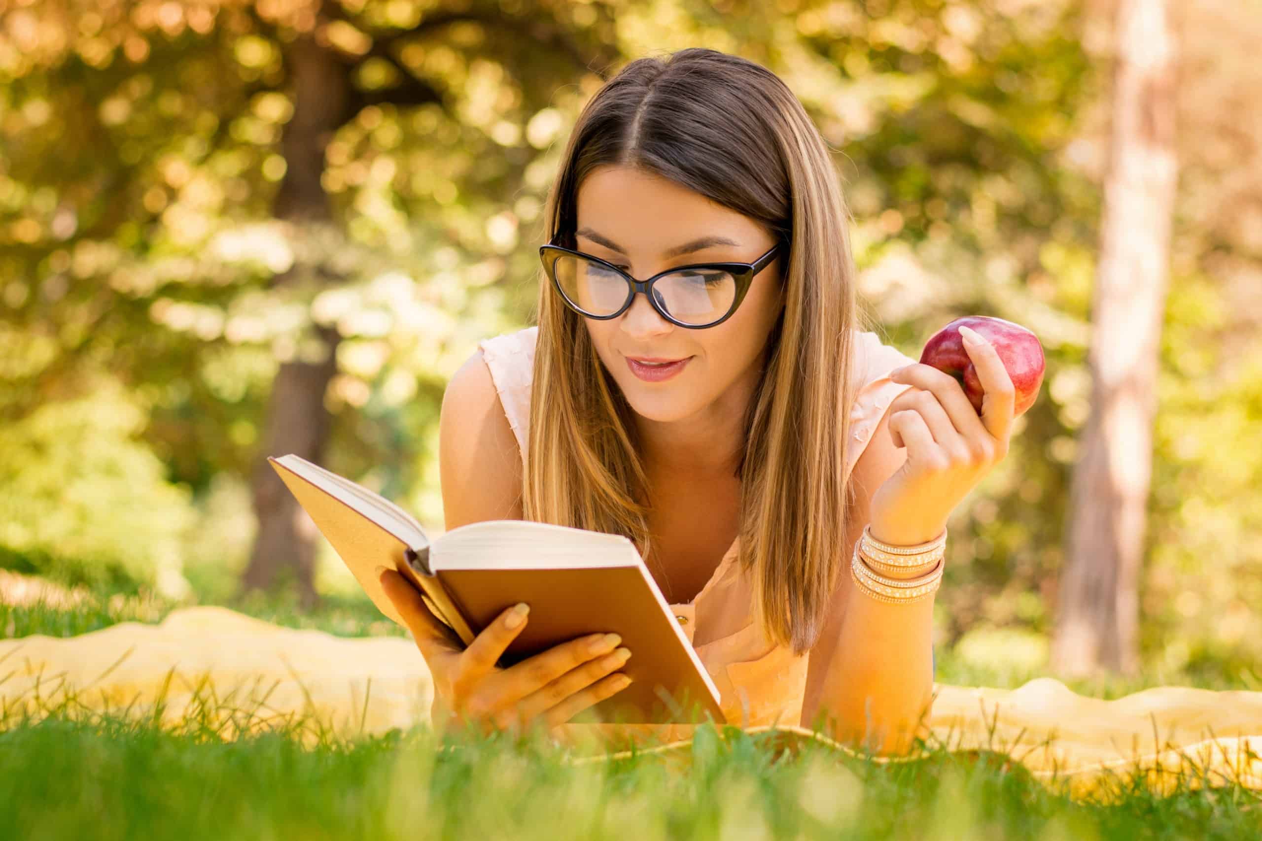 Woman reading a book and holding an apple.