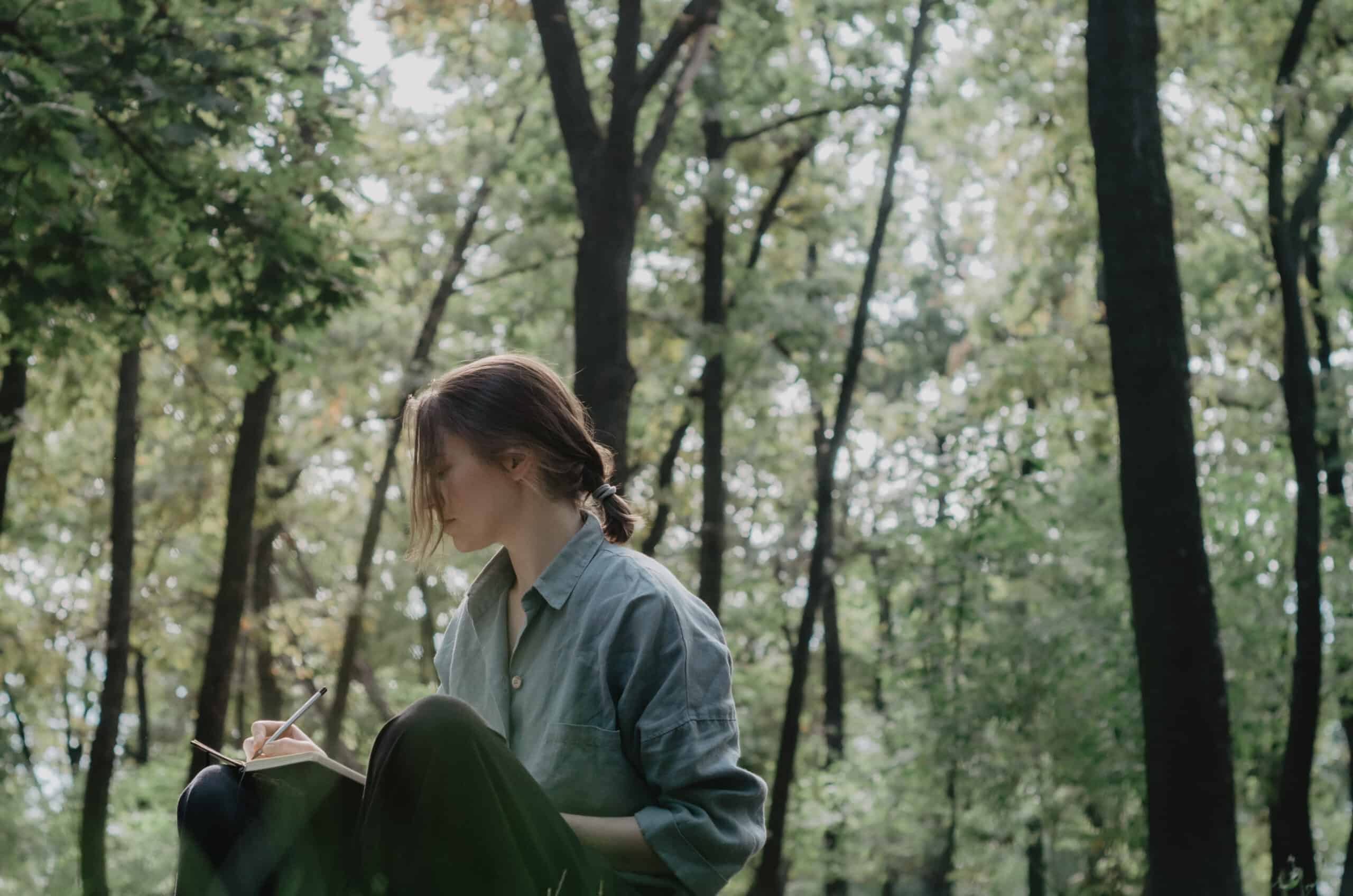 Woman writing in notebook in the middle of the forest