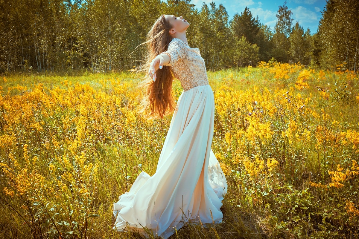 A beautiful tender girl with long blonde hair in a light lace dress enjoys freedom in the autumn field