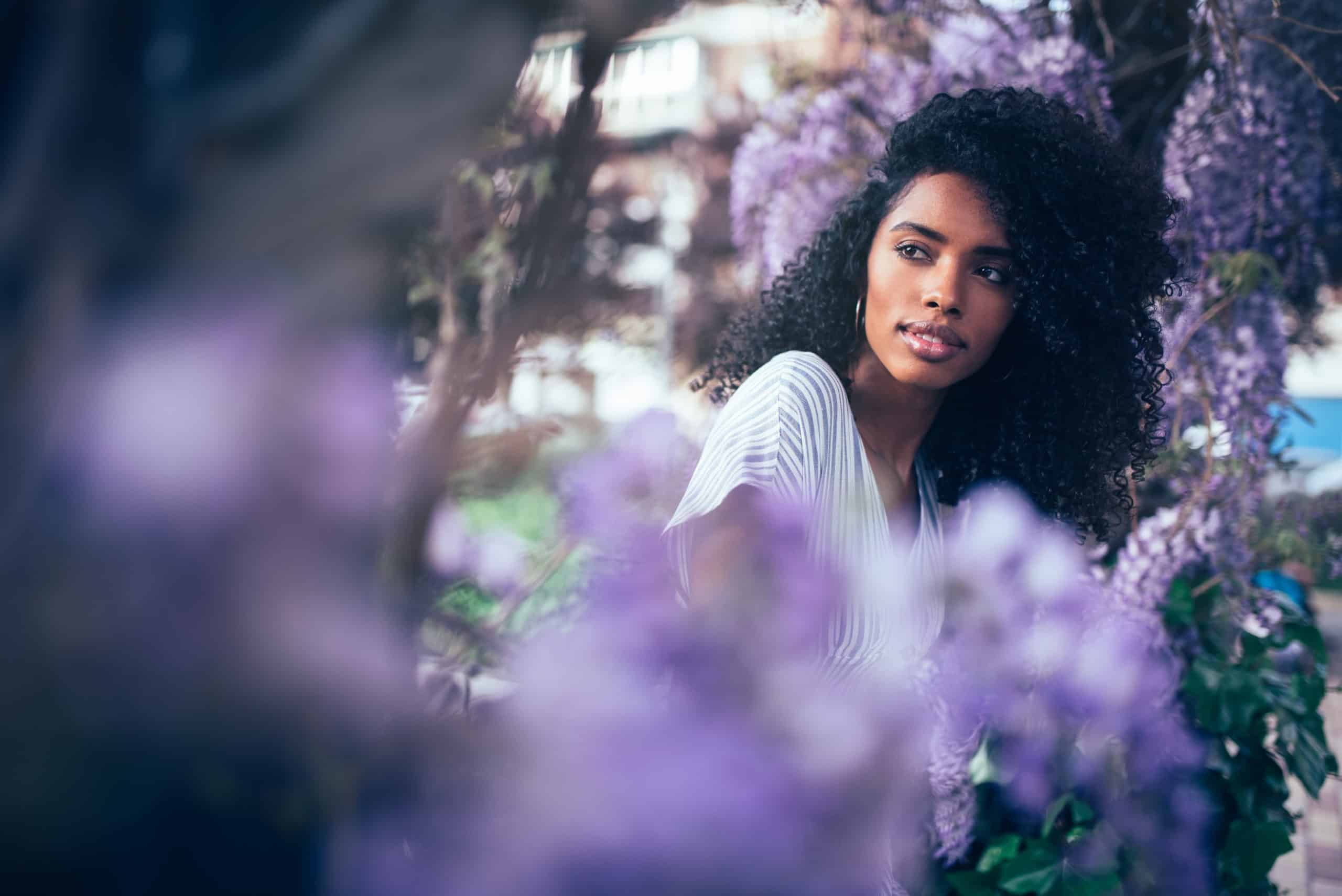 Young attractive black woman sitting surrounded by violet flowers.