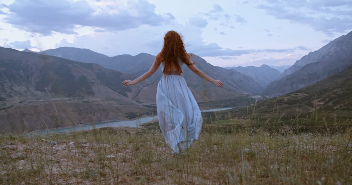 

a woman in white dress runs towards the beautiful view of the mountain and river