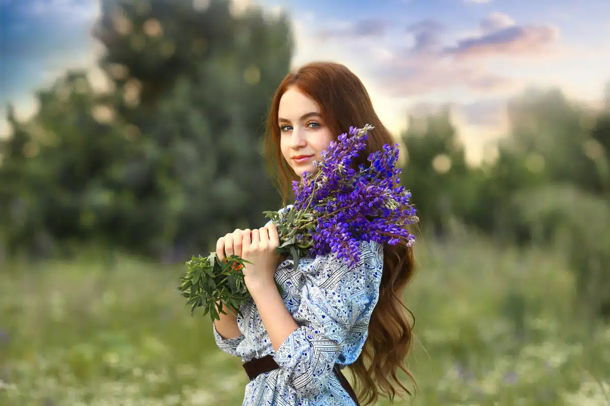 a stunning young girl looking holding a bunch of violet wild flowers in nature