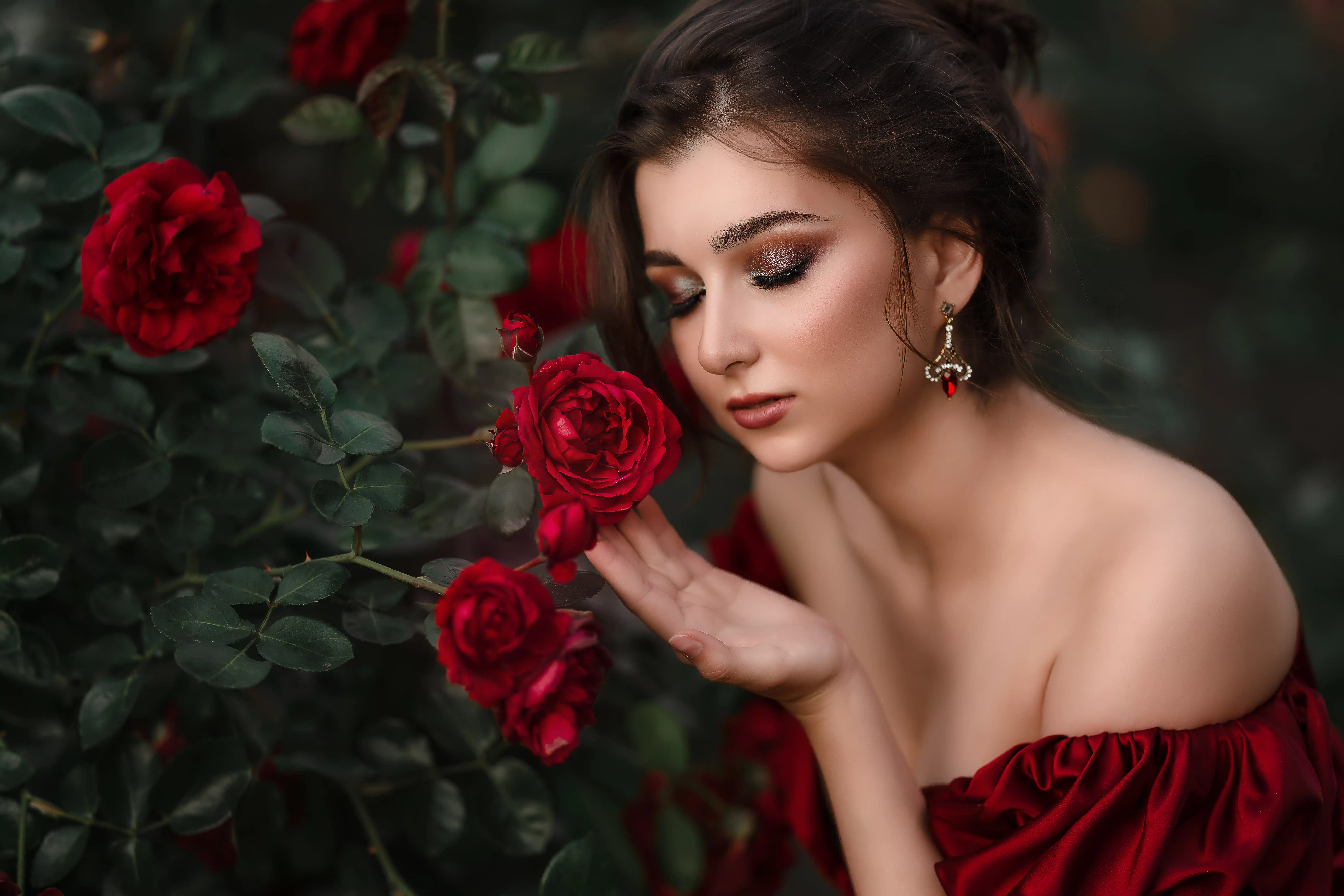 Beautiful woman in red dress walking in the garden full of roses.