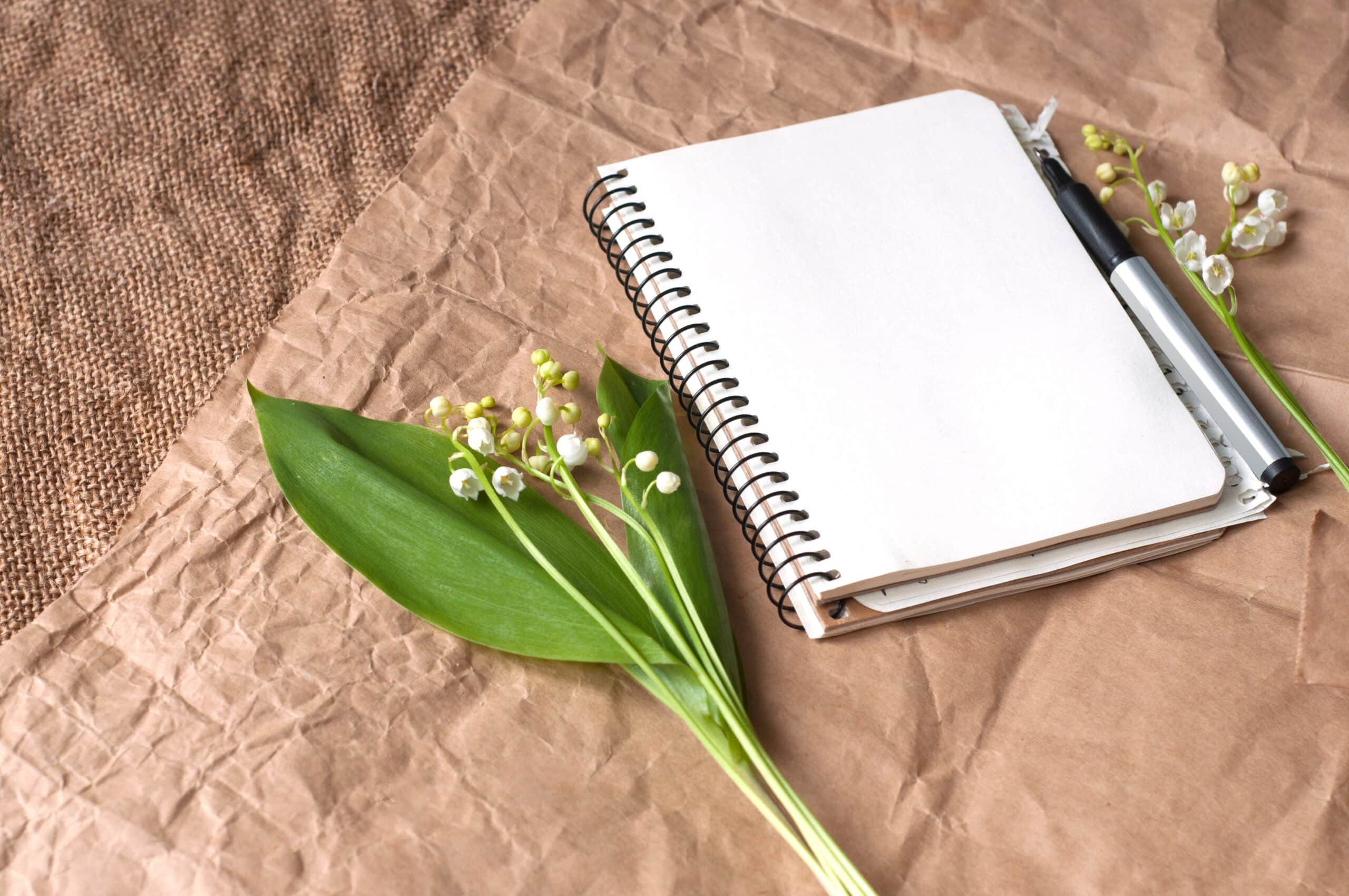 Lily of valleys, blank notepad and pens on sackcloth texture