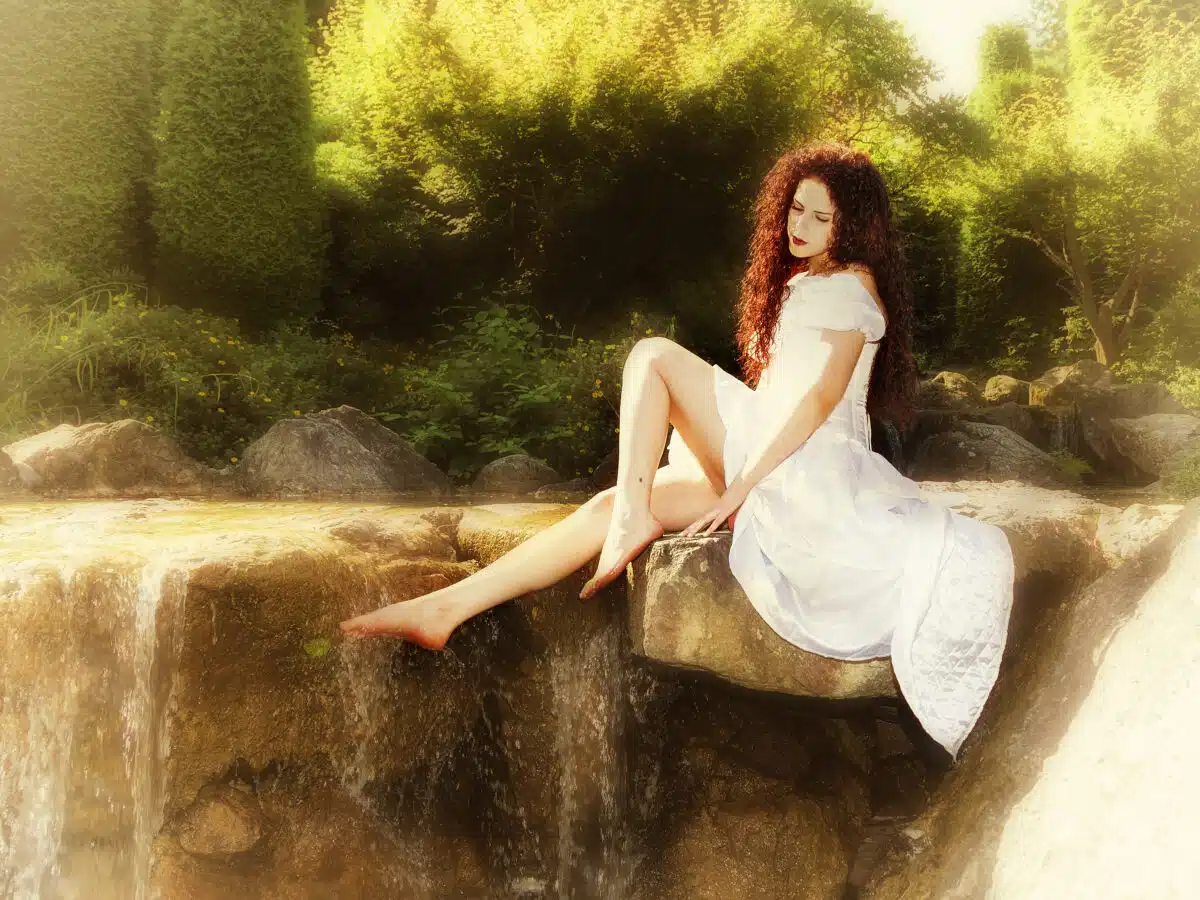 a lady with red curly hair dressed in white is relaxing by the river