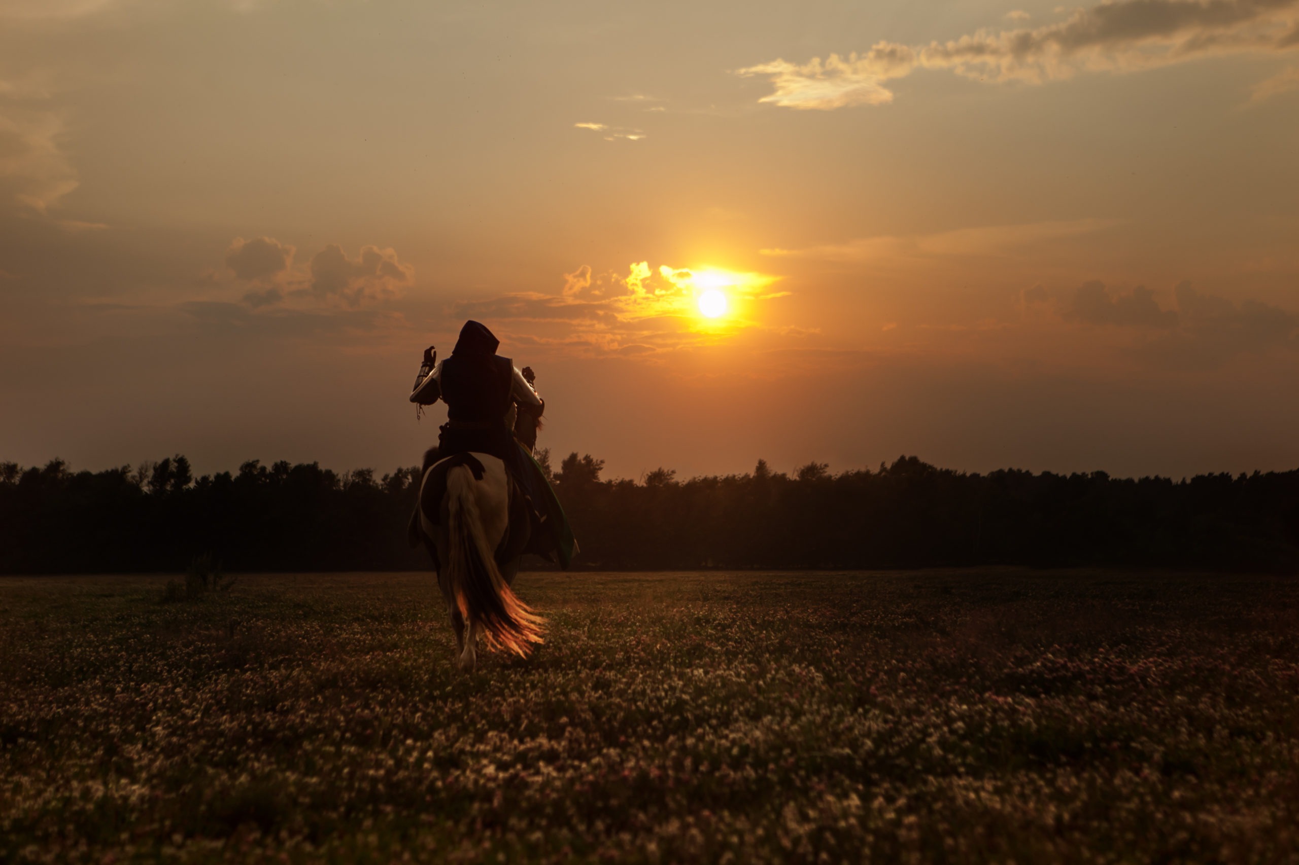 Silhouette of a man on a horse riding toward the sunset.