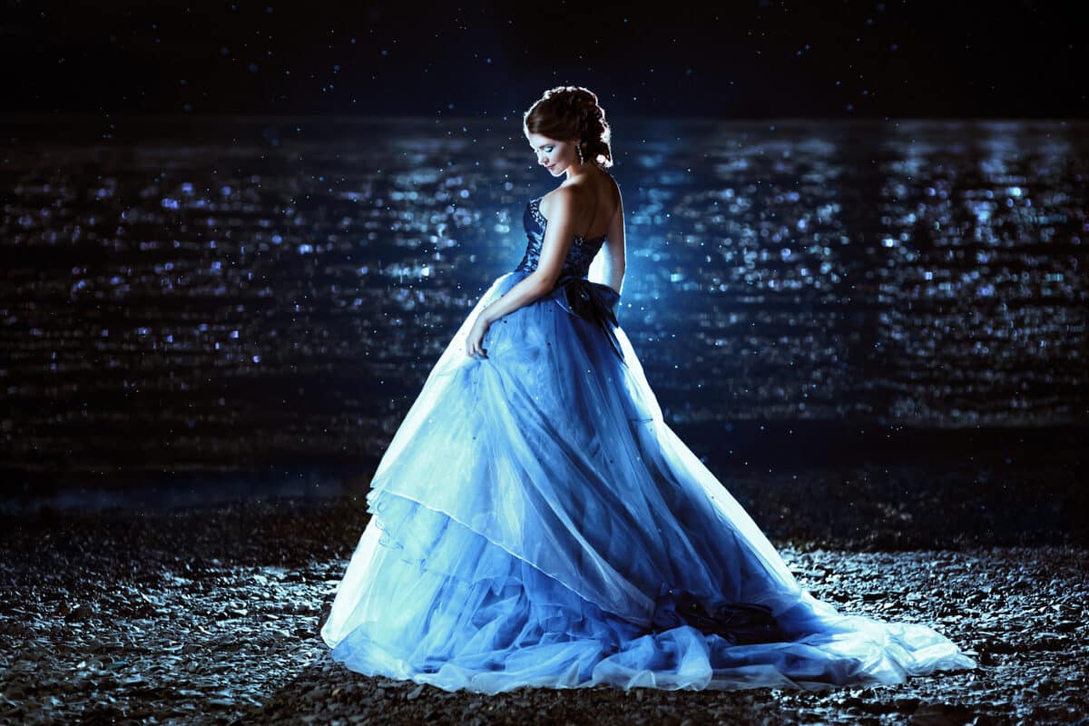 a beautiful lady in blue dress standing on the beach