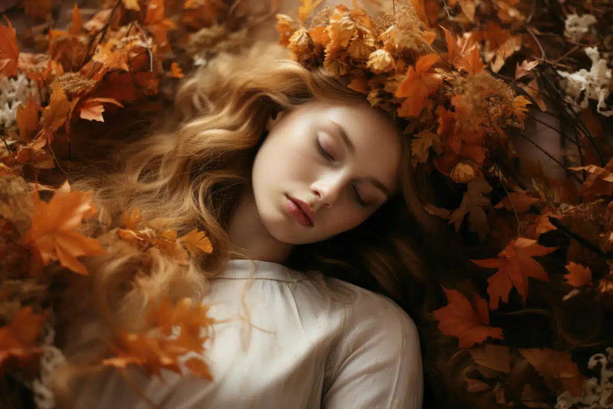 Woman lying down in a bed of autumn leaves, she wearing a white shirt, The leaves are orange, yellow, and brown in color