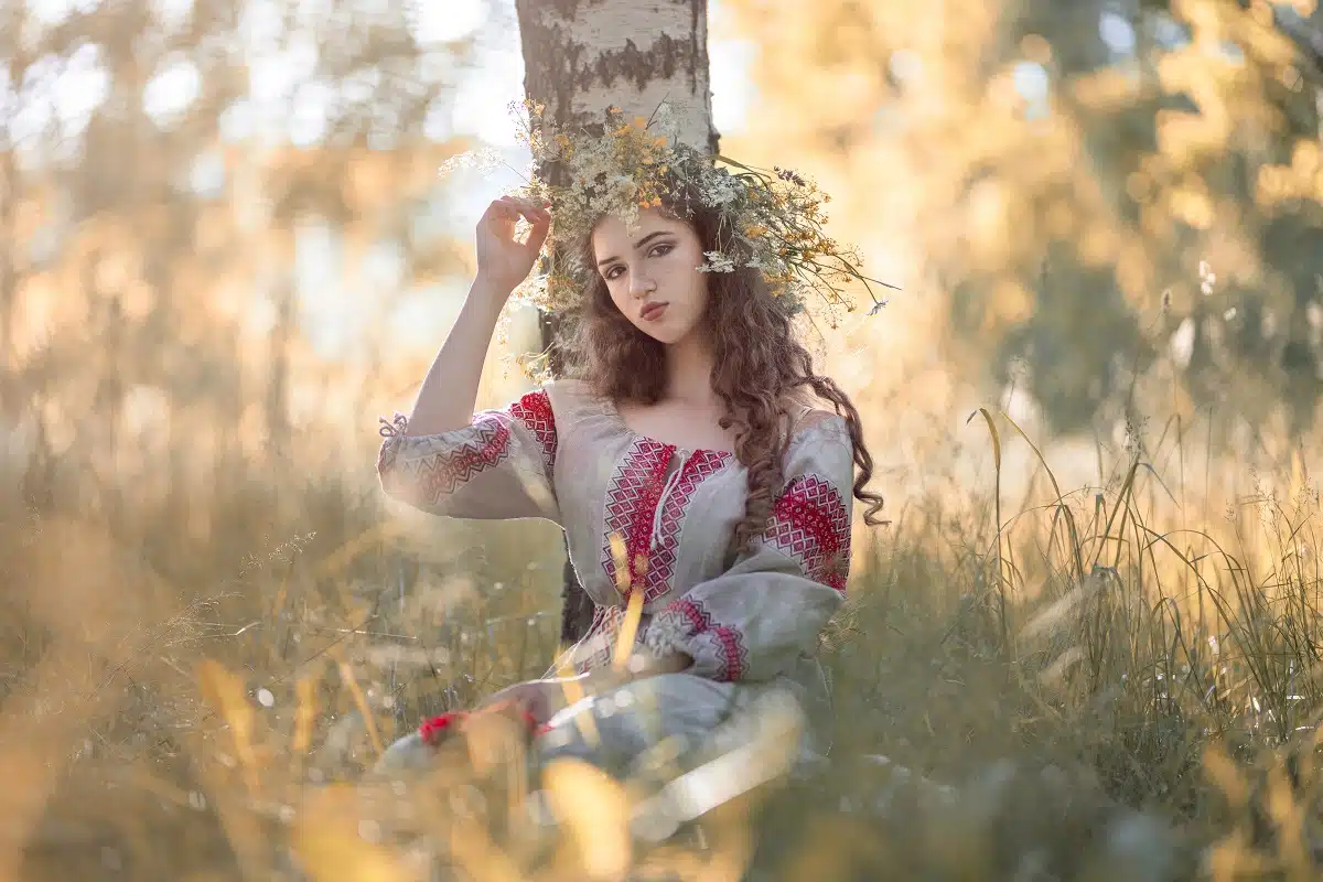 a young lady dressed in traditional clothing and a wreath as she relaxes in the woods
