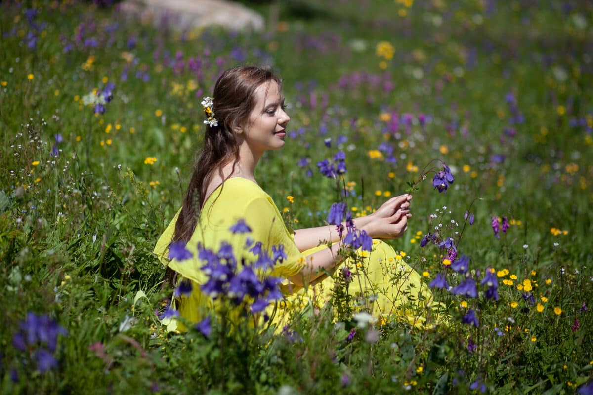 A pretty girl in a yellow dress relaxing in a flowering field on the mountain