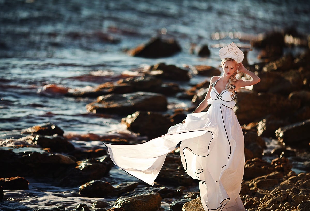 a lady in white fluttering dress on the rocky beach