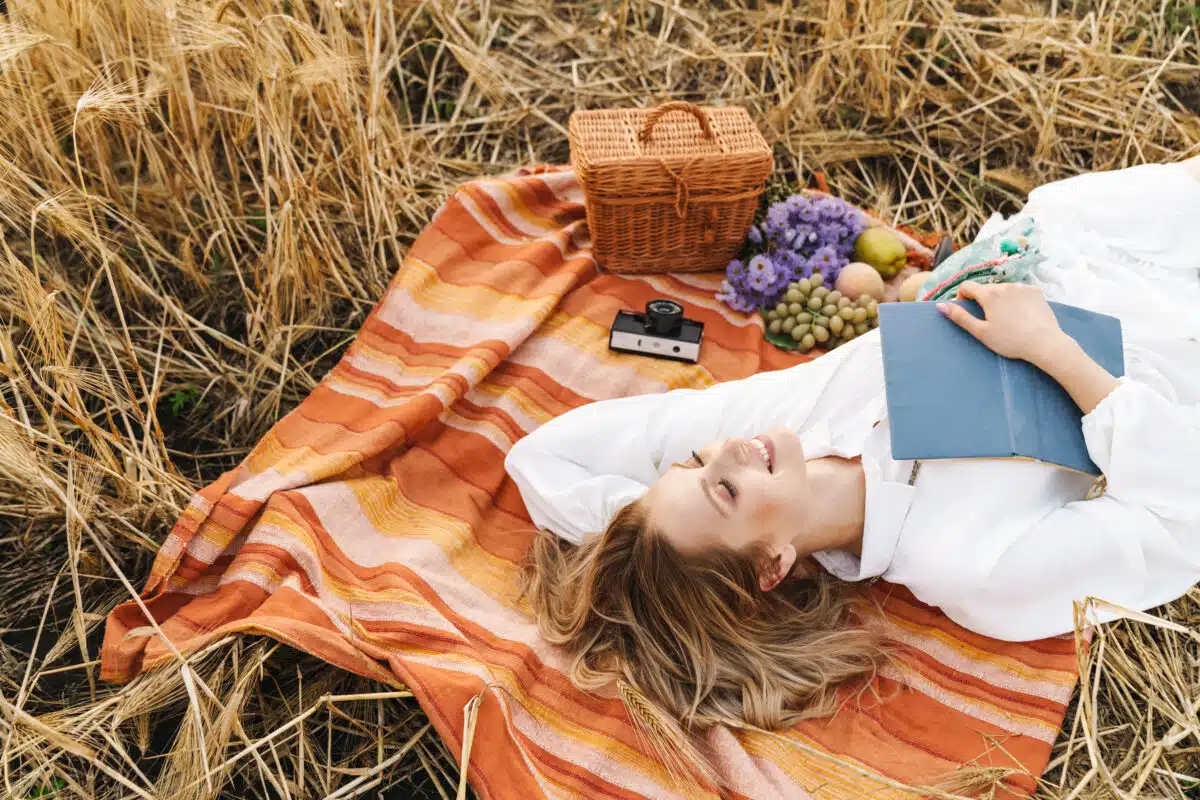Image of young blond woman lying on blanket with book in golden field