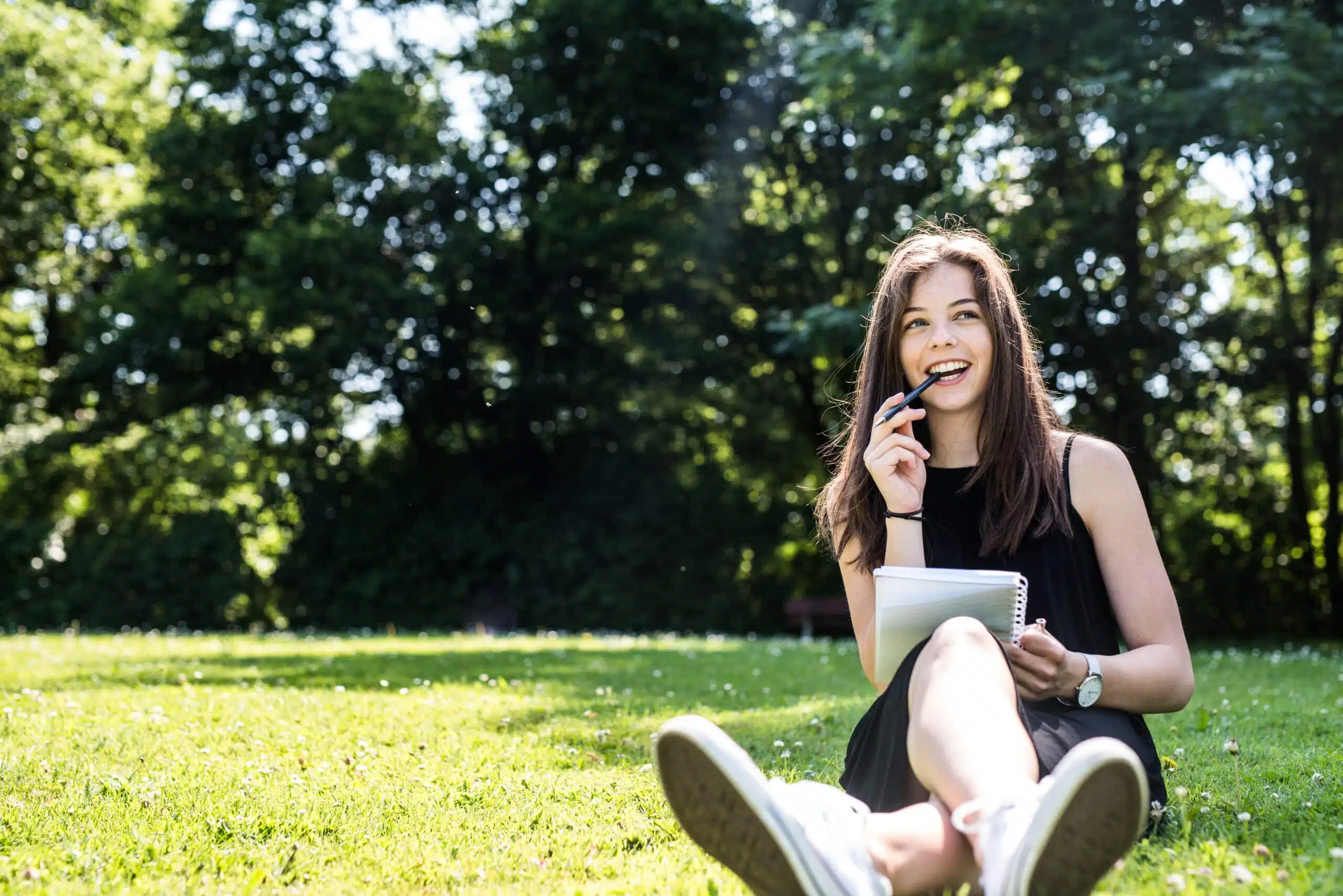 Young cheerful woman writing outdoors on the grass.