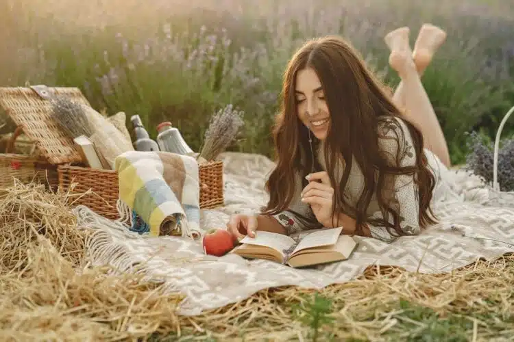 Woman in a lavender field sitting on a blanket reading a book
