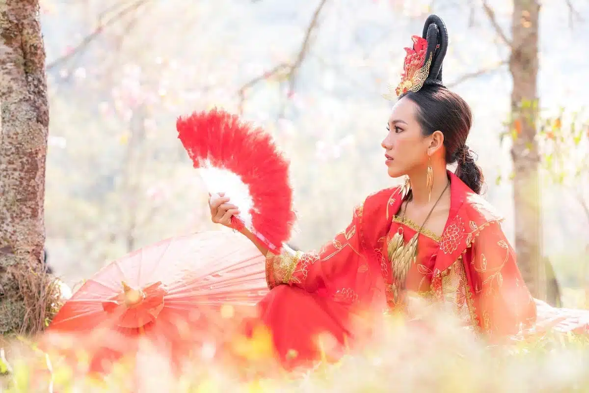 Chinese woman outdoors in ancient chinese dress and red feather fan.
