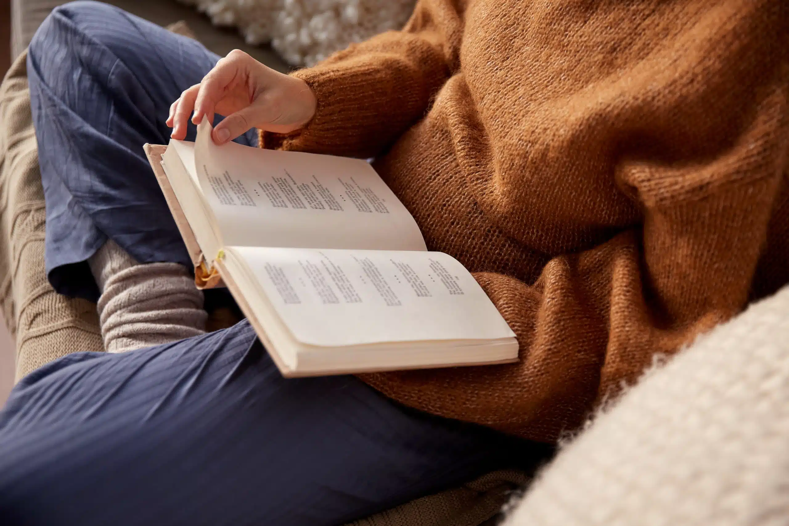 woman in warm sweater reading a poetry book at home