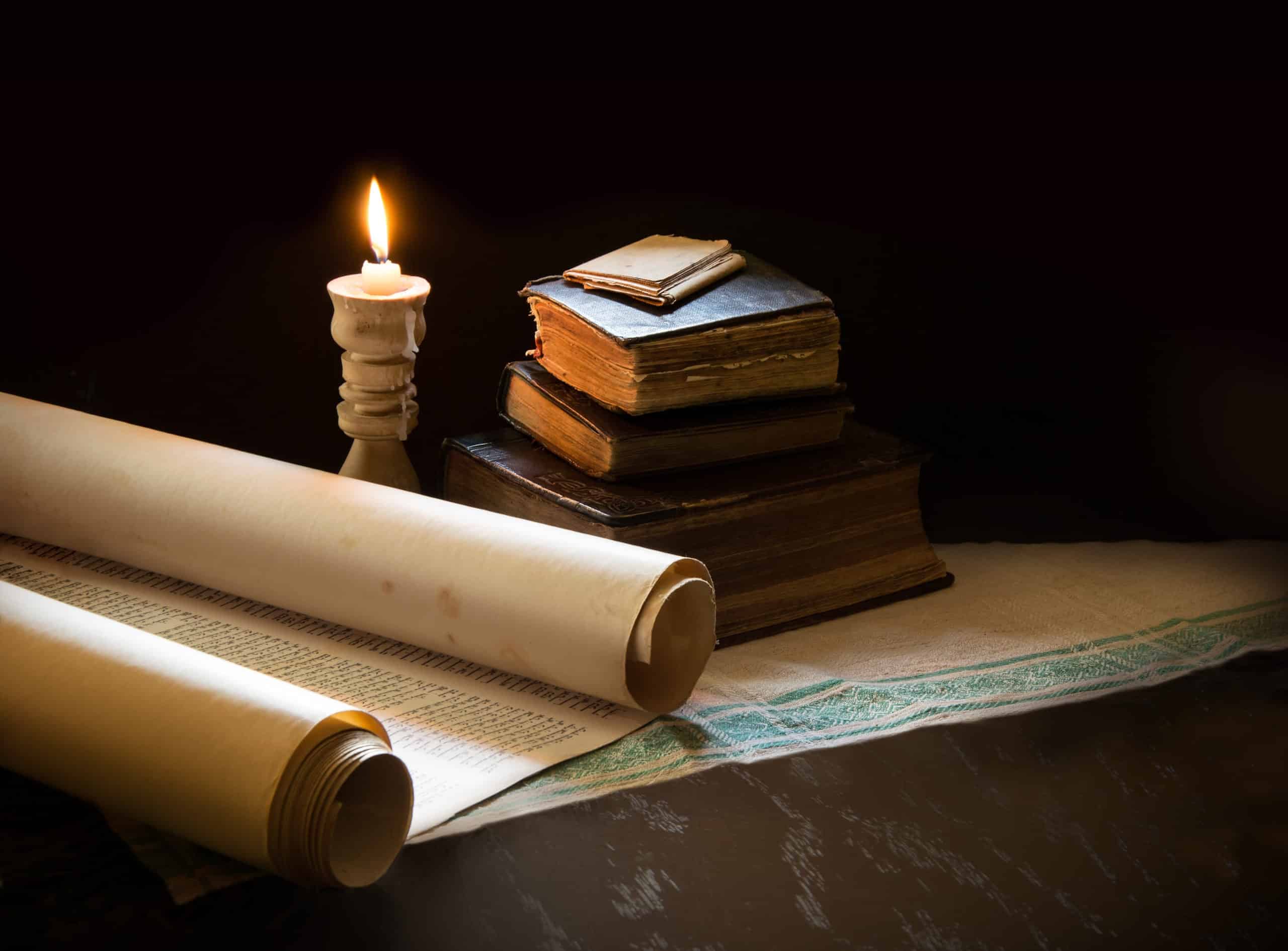 Ancient books with a lit candle and a scroll.