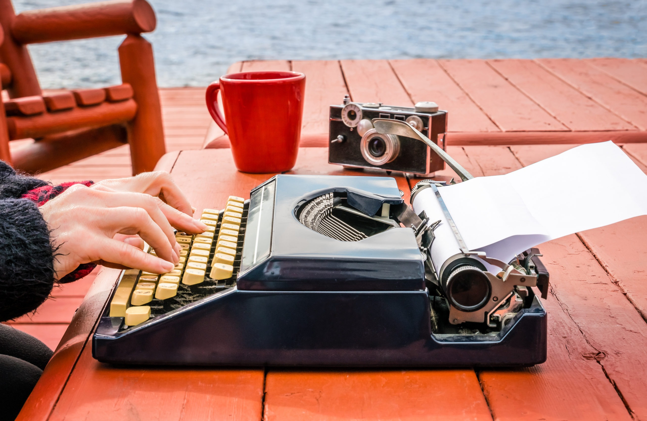 Female hands typing on a vintage typewriter outdoors at wooden desk.