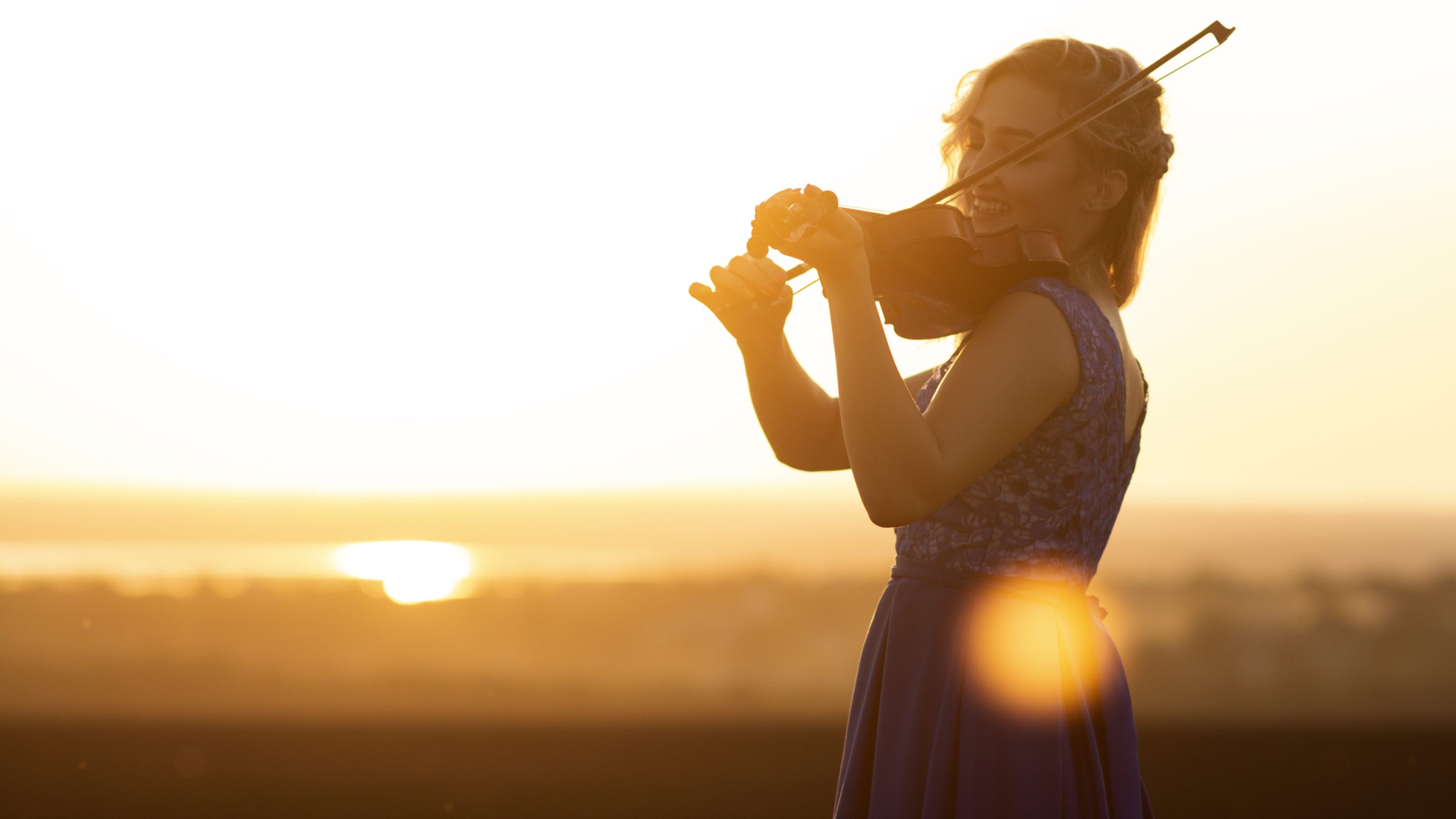 silhouette of a female figure playing the violin at sunset