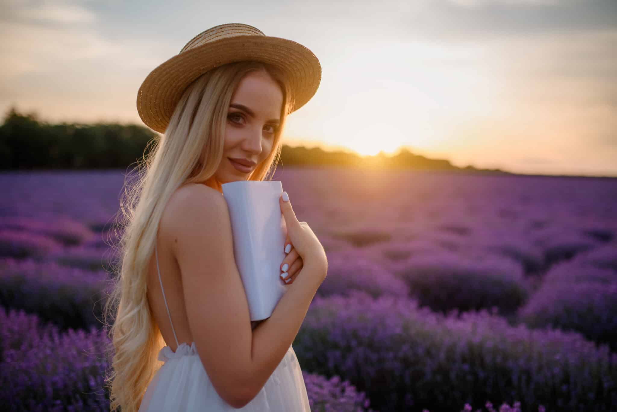 Young beautiful woman in white dress and hat is walking in a lavender field