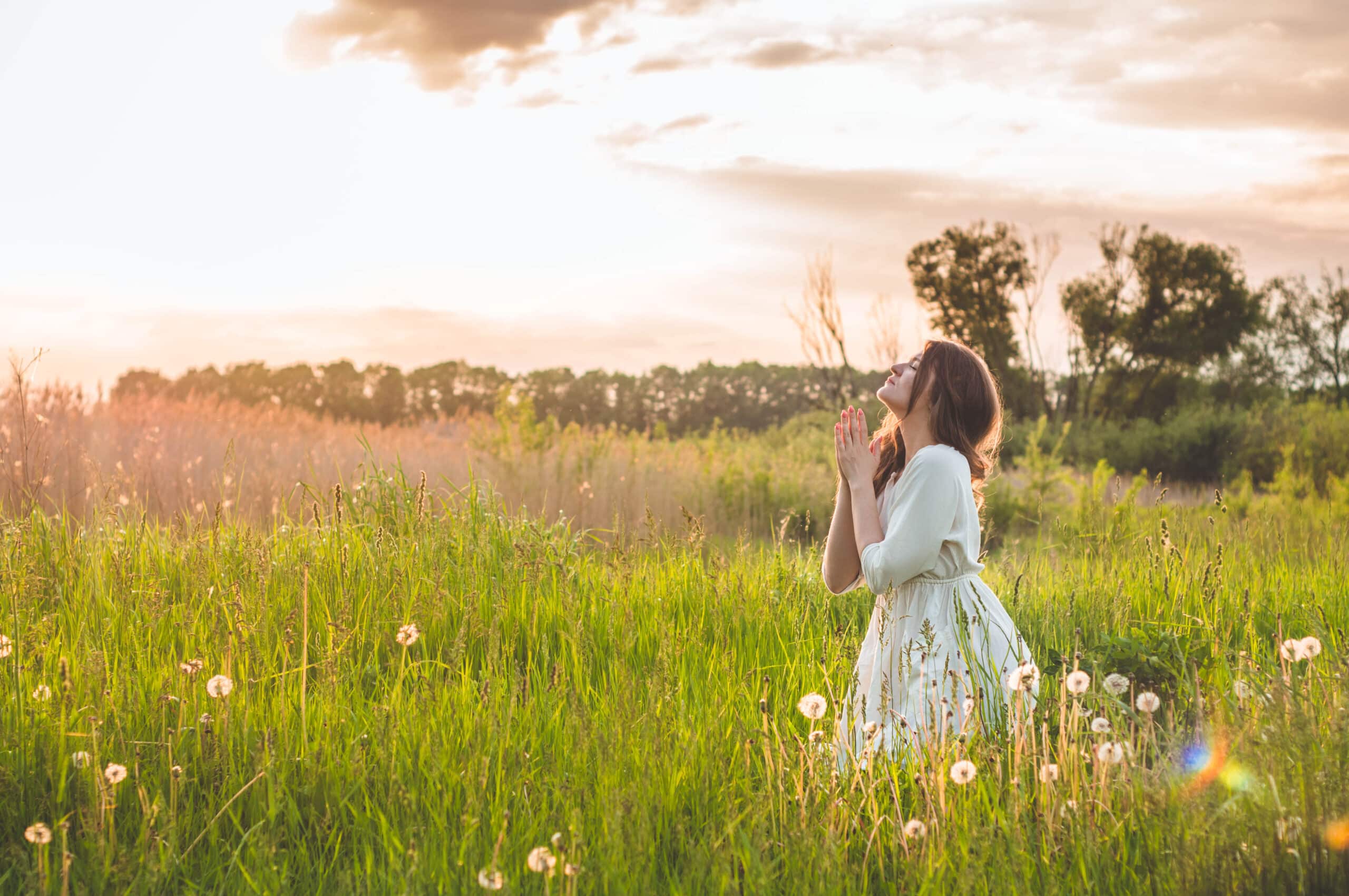 Girl closed her eyes, praying in a field during beautiful sunset