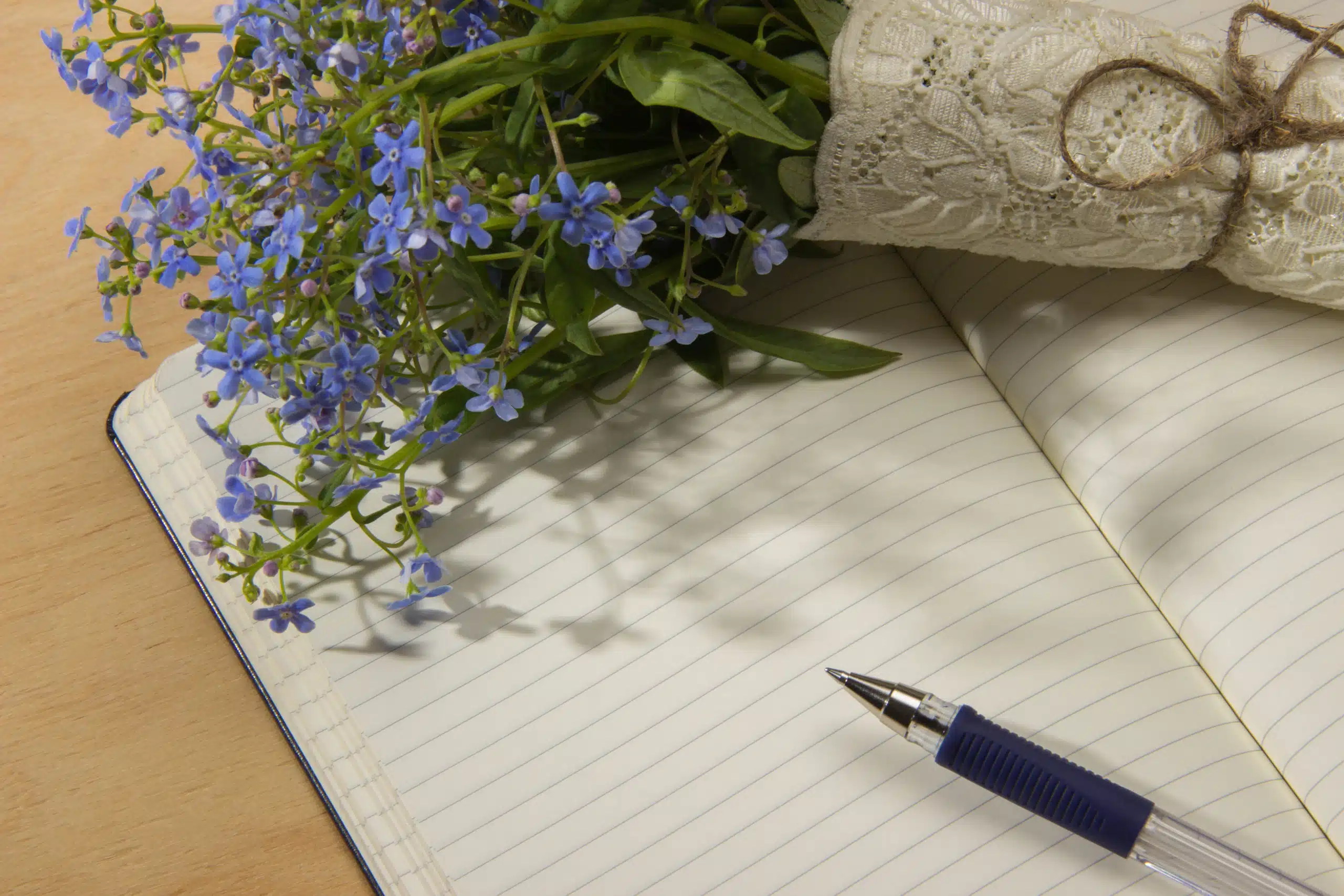 A bouquet of forget-me-not flowers, notebook and pen on the wooden table.
