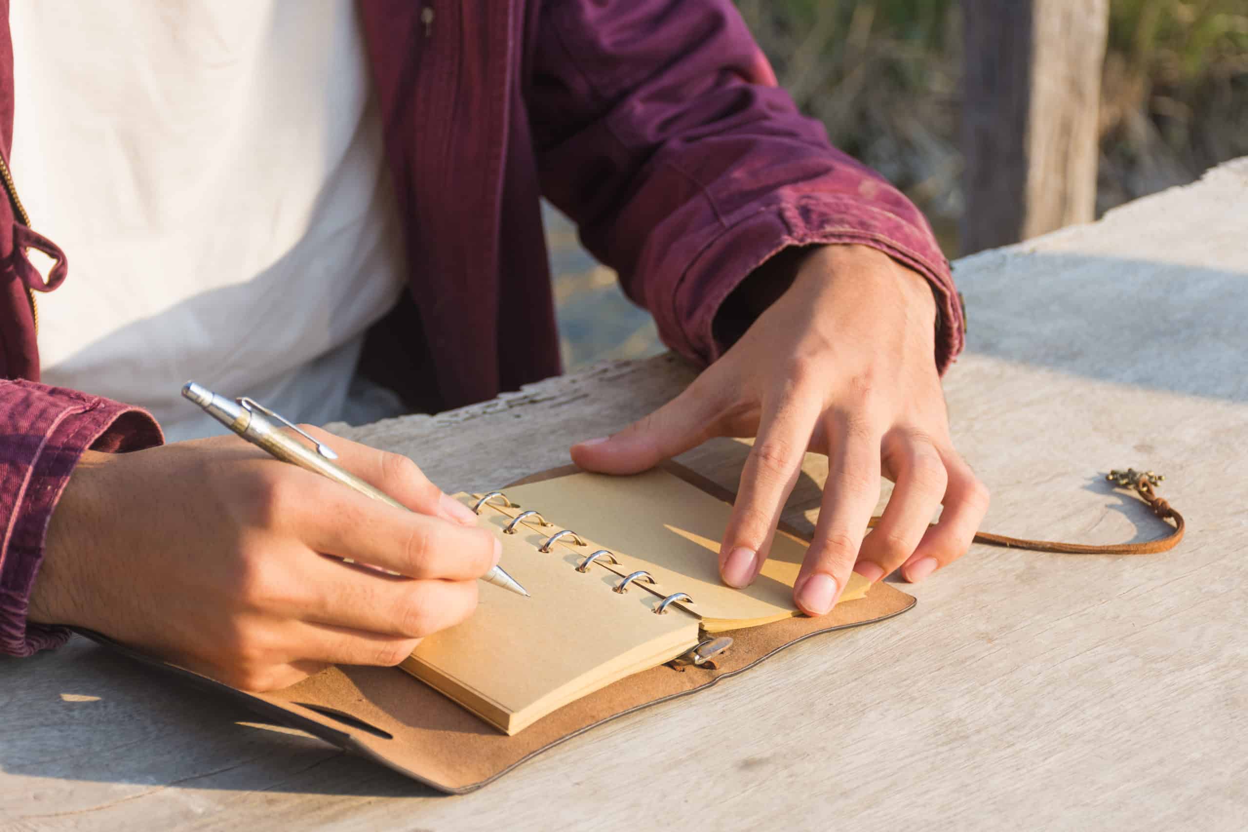 Male hand writing in notebook on a wooden table.