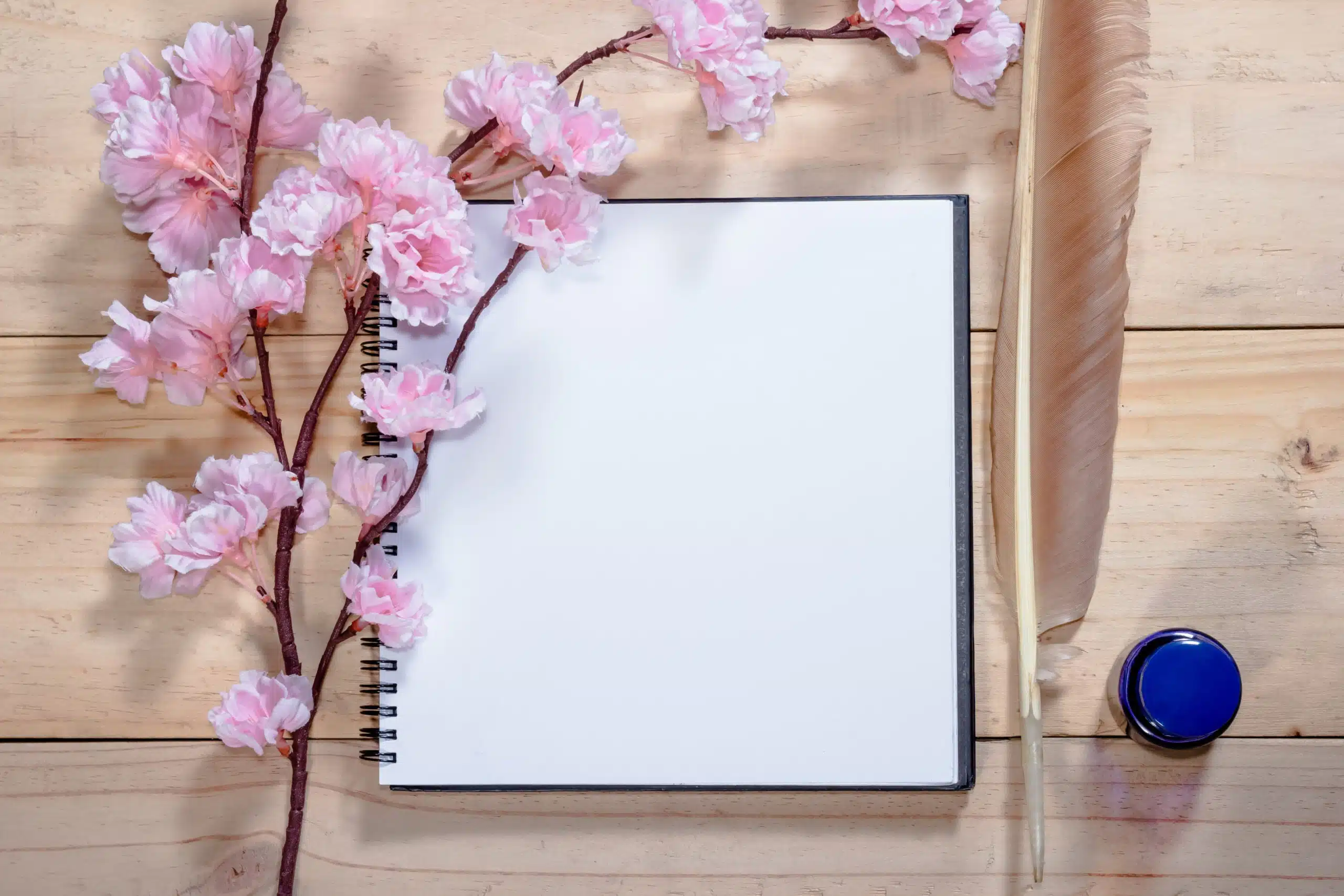 Open note book with quill pen, inkwell and pink sakura flowers on wooden background