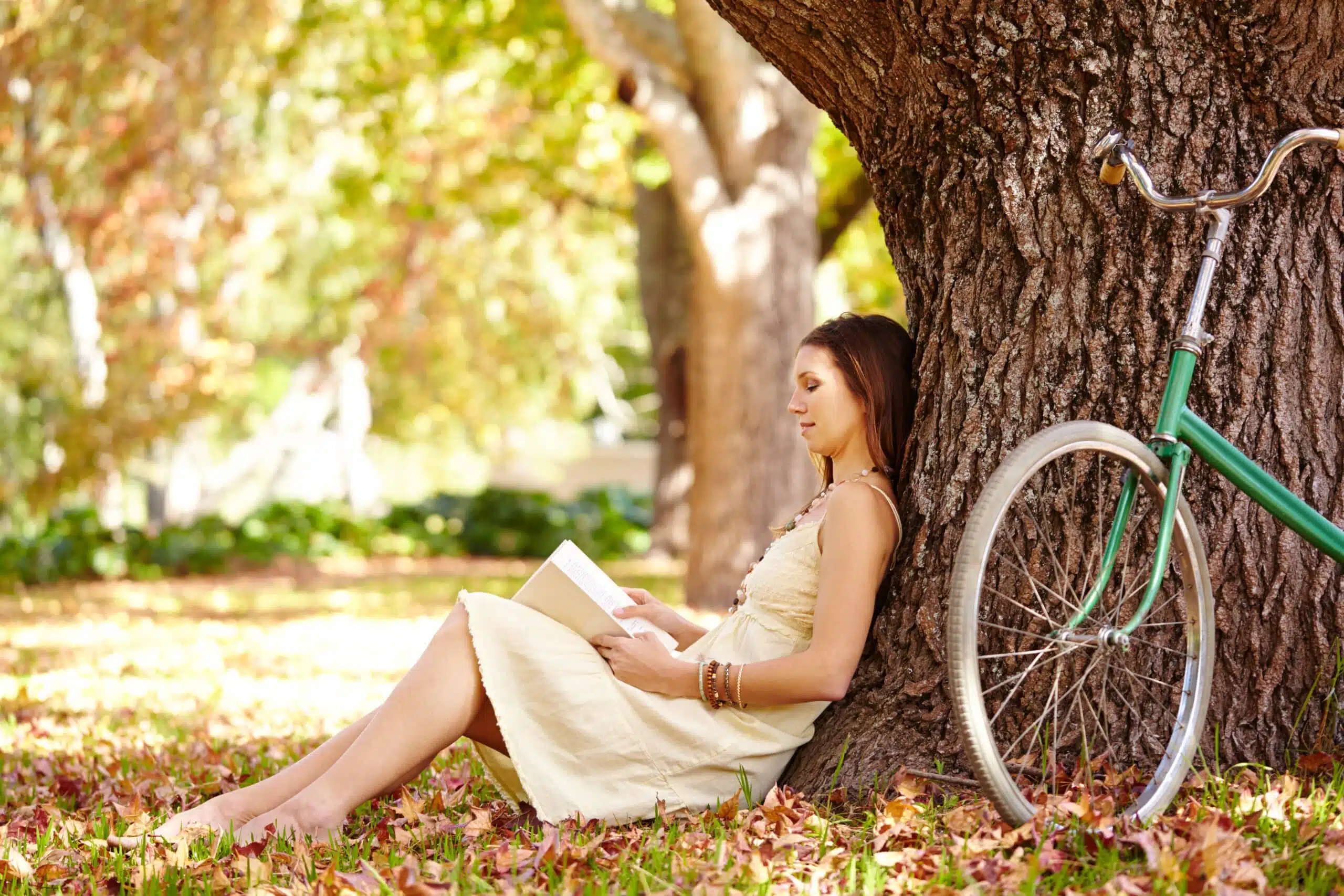 Woman leaning on a tree and sitting on the ground reading a book