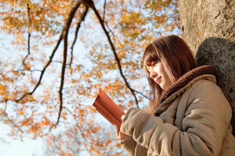 Attractive Asian woman reading a book outdoor in nature.