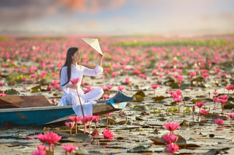 Beautiful  Vietnamese woman in traditional dress sitting on a boat in lake with lotus flowers