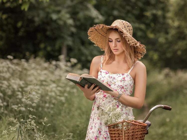 a girl in a sundress with a hat and a bicycle reads a book