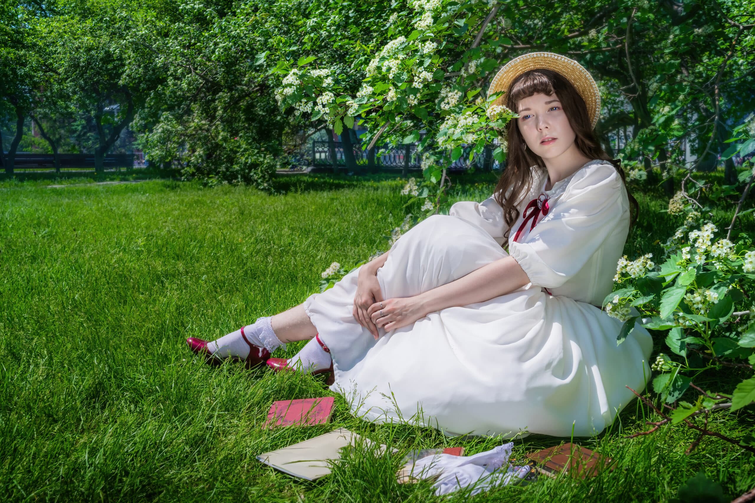Nice girl in a white dress sits on a lawn in a park, books and notebooks spread in front