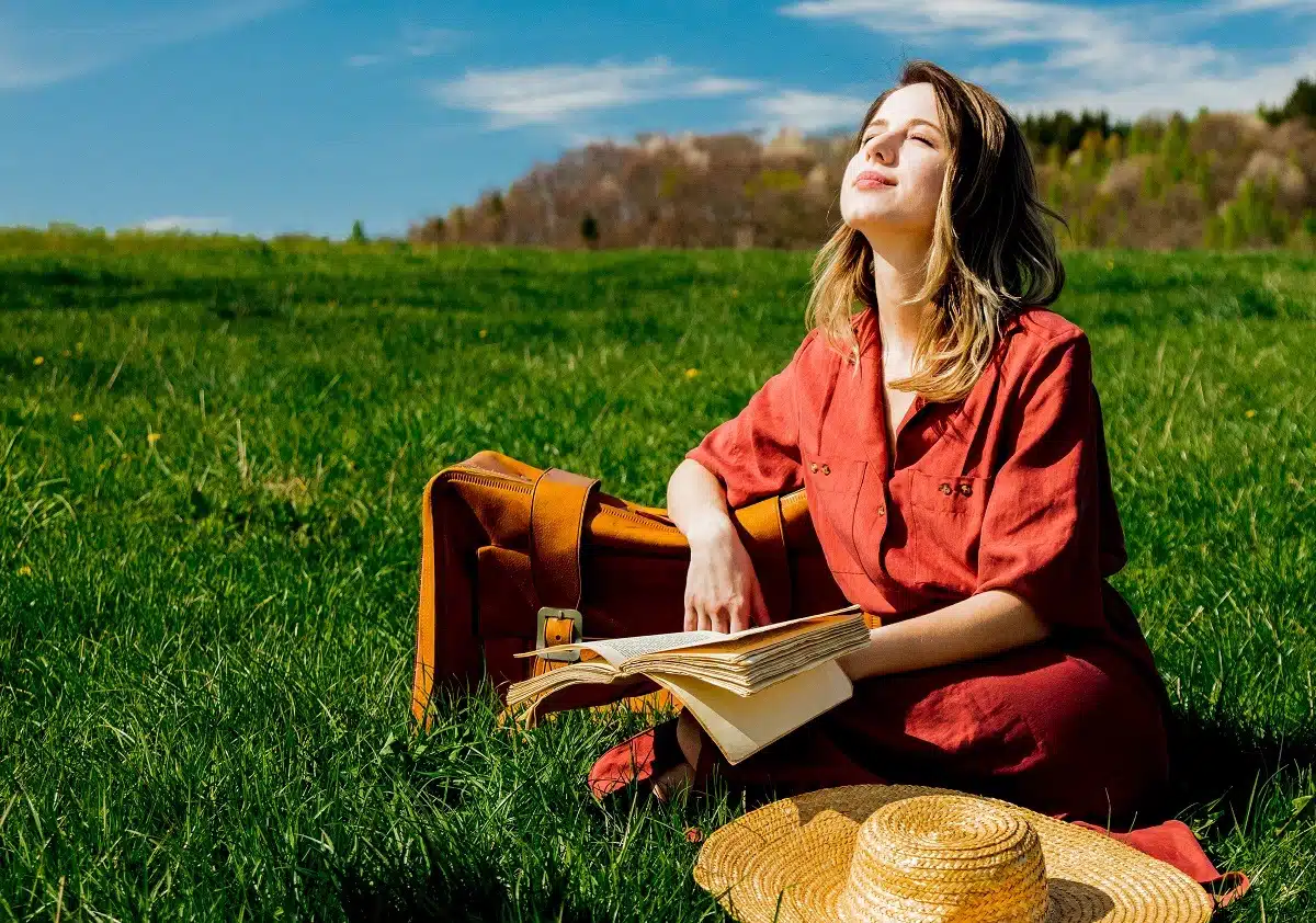 Beautiful girl in red dress and hat with suitcase and book at the meadow