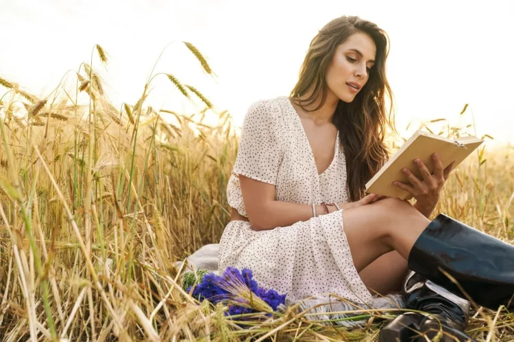 focused woman reading book while sitting on wheat field
