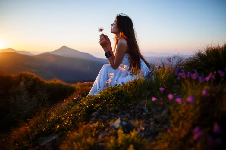 A girl in white dress sits on the edge of the cliff with wild flowers 
