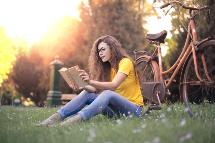 young woman reading a book outdoors on the grass
