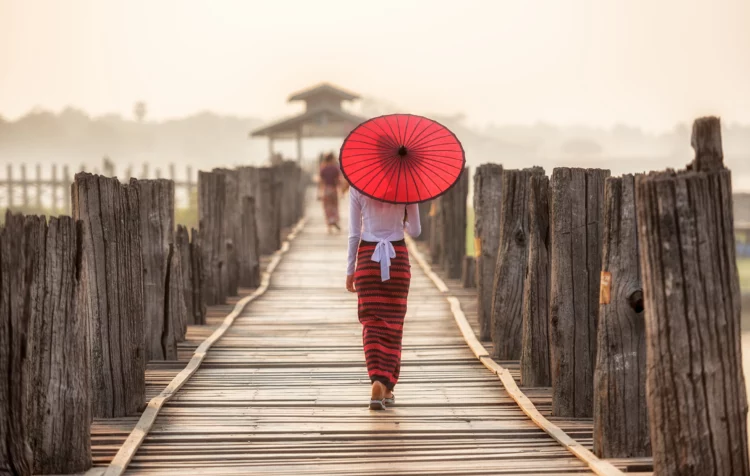Burmese woman holding traditional red umbrella and walking on U Bein Bridge, Myanmar