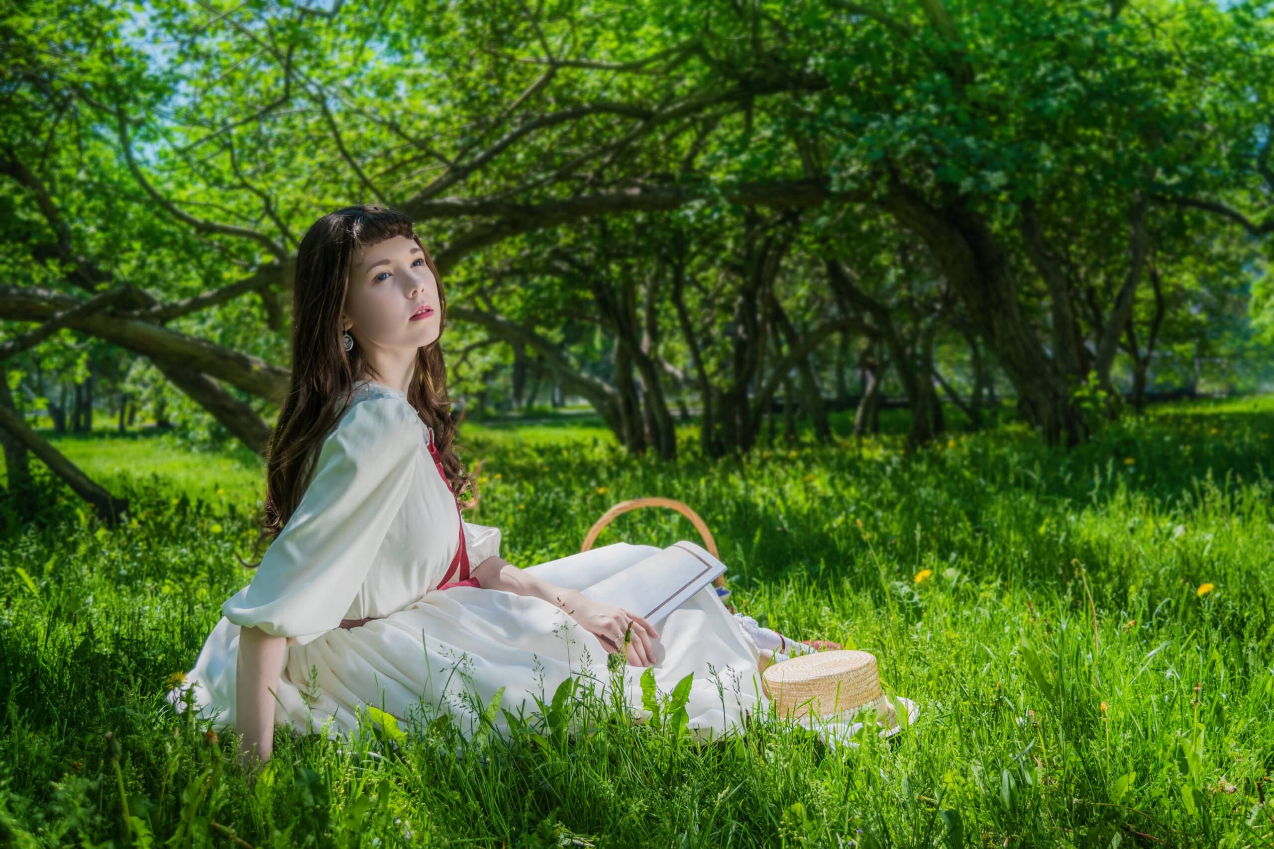 young lady in a white dress sitting on the grass under a tree