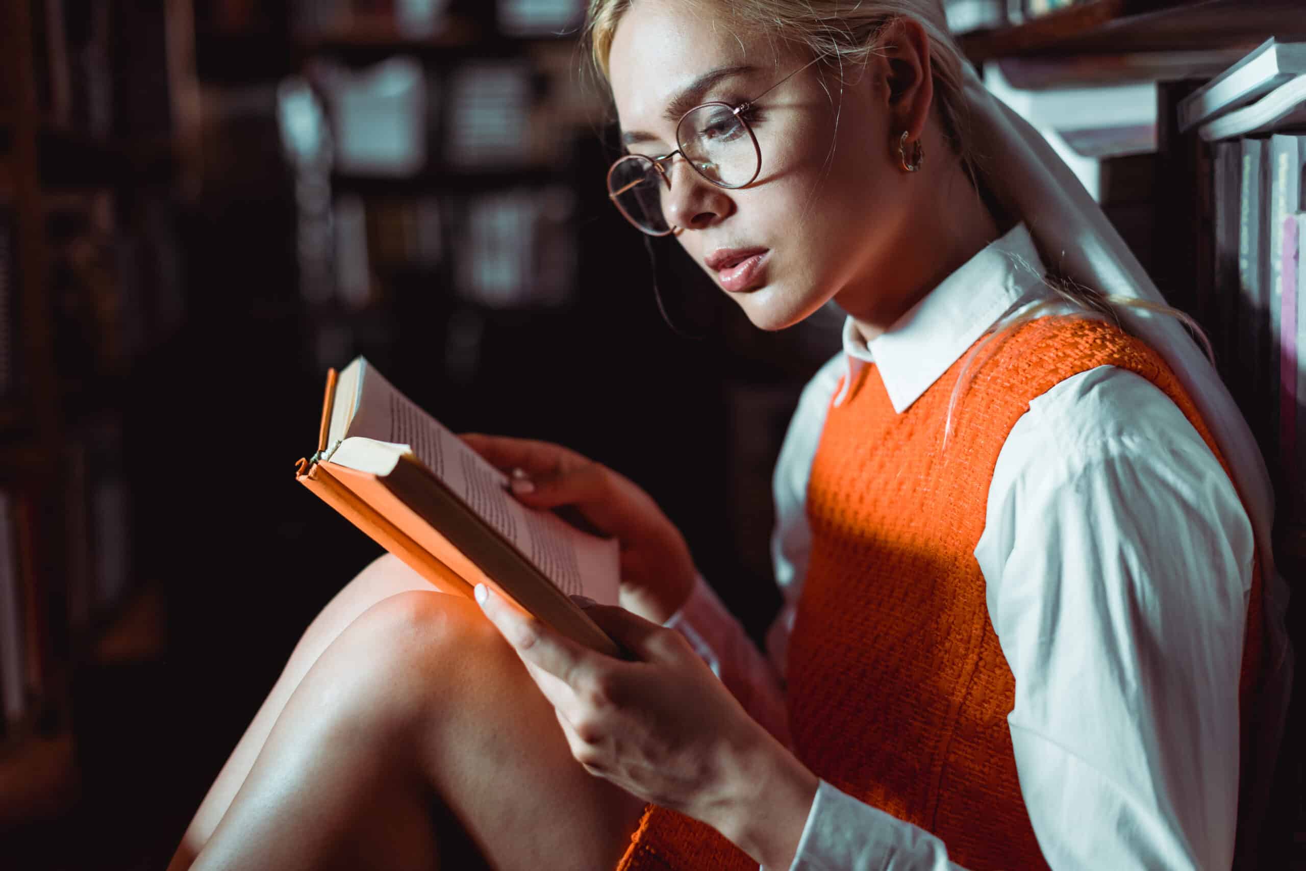 beautiful blonde woman in glasses reading a book in the library