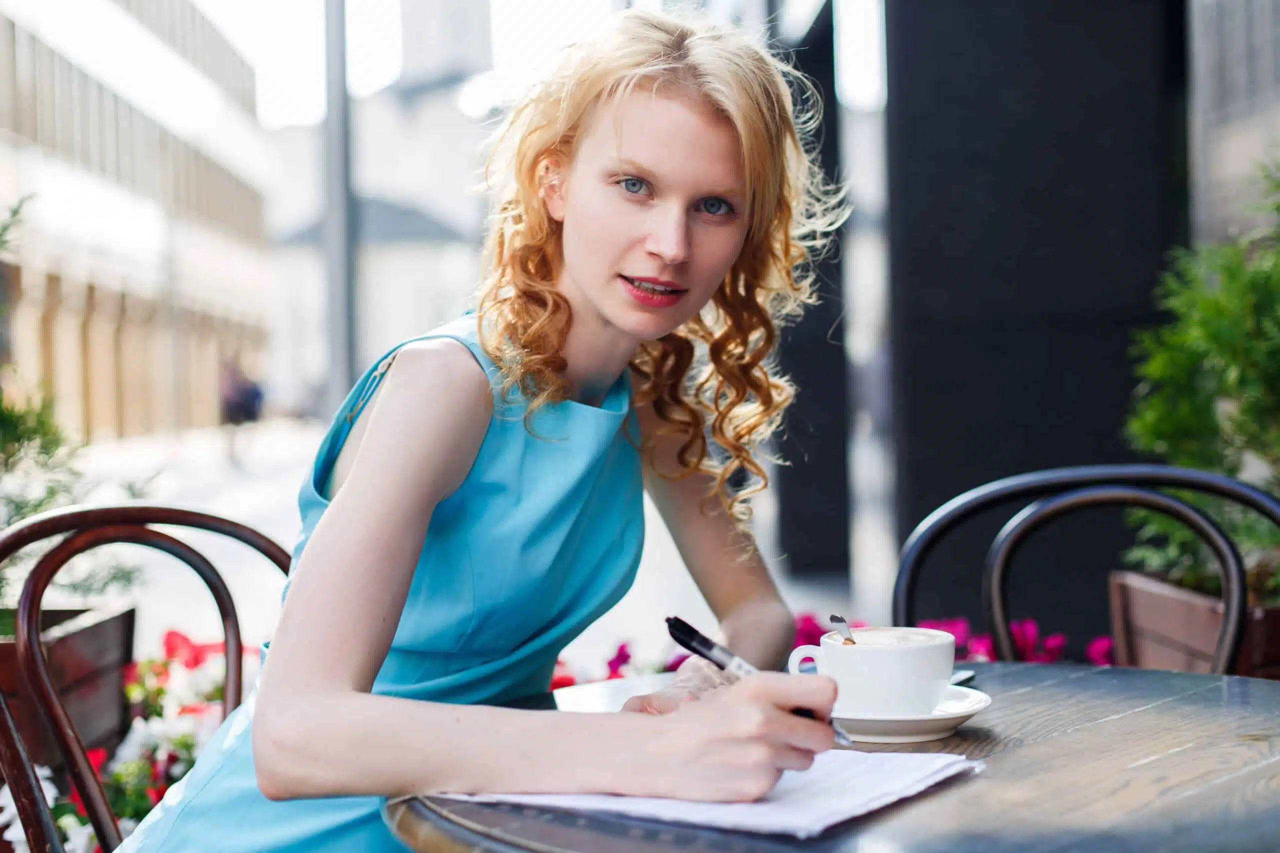 Young woman in elegant blue dress writing in cafe